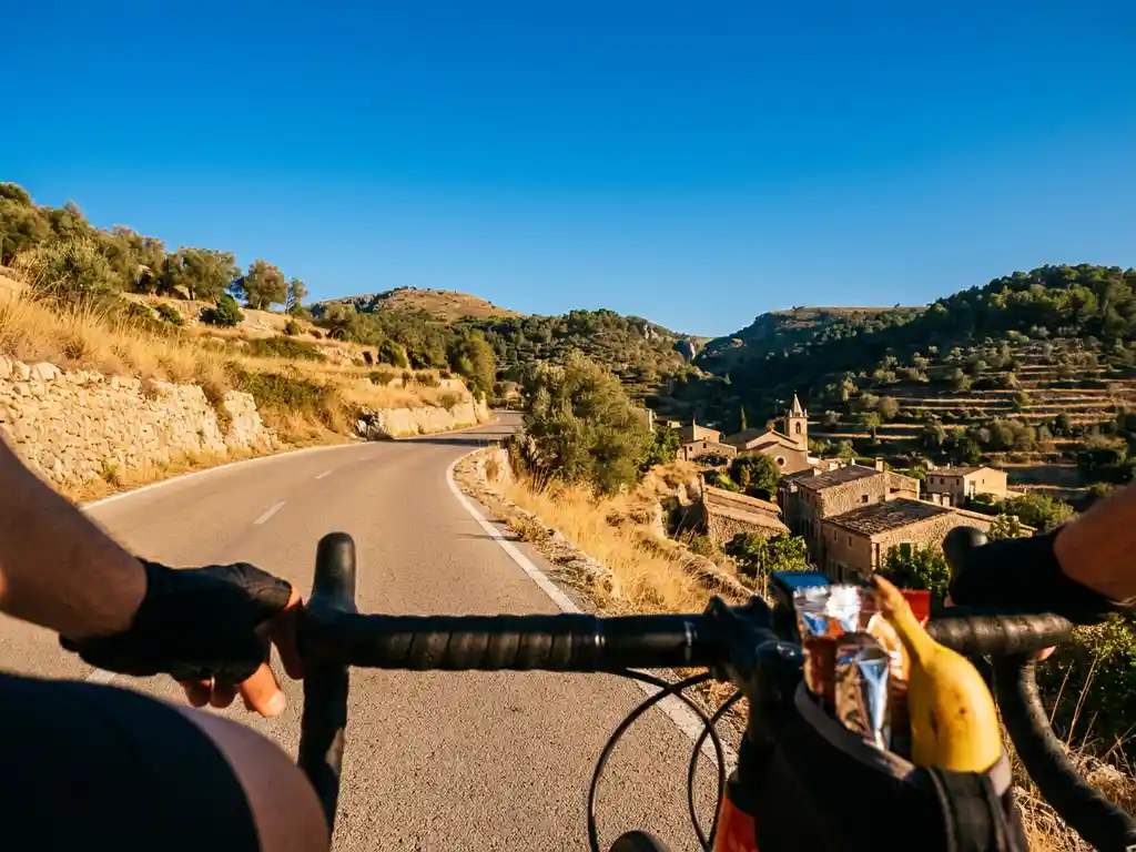 Radfahrer-Perspektive auf kurvenreiche Bergstraße in Mallorca mit goldenem Terrassengelände, Trikottasche mit Energieriegeln im Vordergrund.